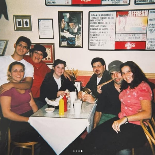 A group of seven people, including a family, smiling and posing around a table in a casual restaurant.