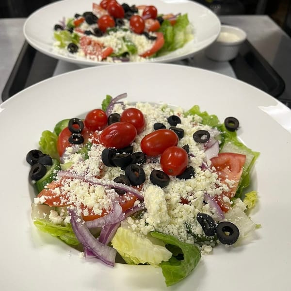 Two plates of fresh salad with lettuce, tomatoes, olives, red onion, and crumbled feta cheese.