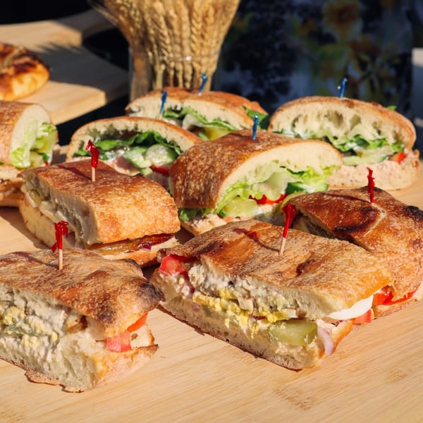 Assortment of fresh sandwiches with various fillings, including egg salad and deli meats, on a wooden board.