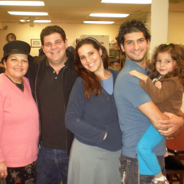 A family of five, including a young girl, smiling together indoors under fluorescent lights.