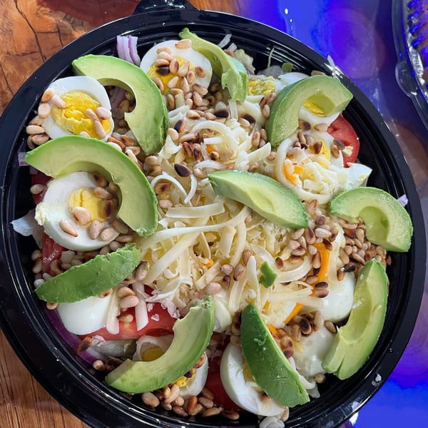 A vibrant salad with avocado slices, hard-boiled eggs, shredded cheese, and pine nuts.