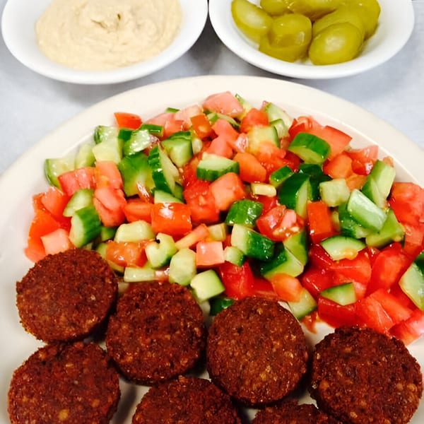 Falafel patties with a side of diced tomato and cucumber salad, hummus, and pickles.