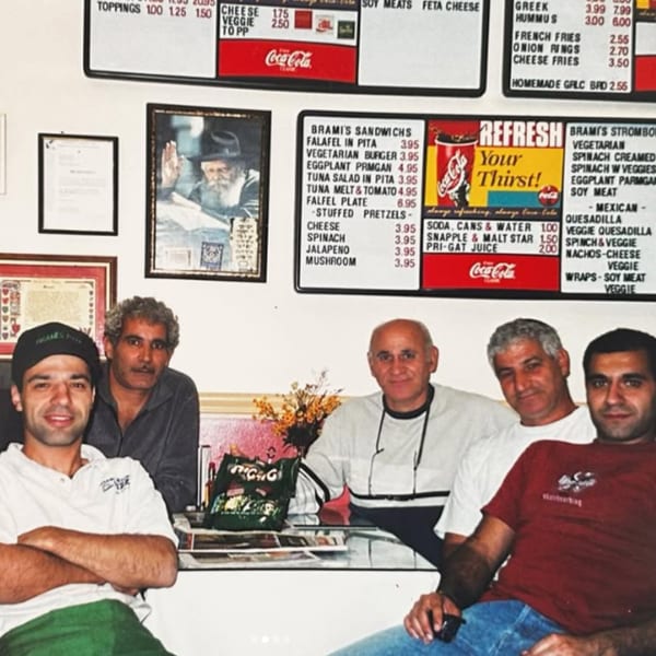 Five men smiling at the camera, seated at a table in a casual restaurant with menus on the wall.