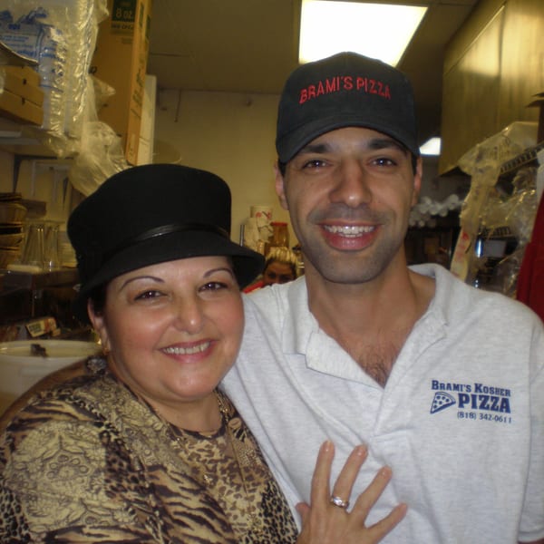 A smiling man in a "Brami's Pizza" hat and shirt with a woman in a black hat.