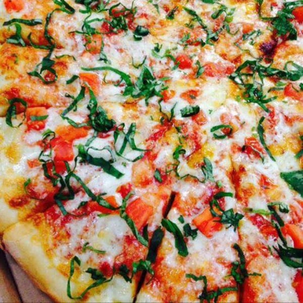 Close-up of a Brami's Kosher Pizza with melted cheese, diced tomatoes, and fresh basil.
