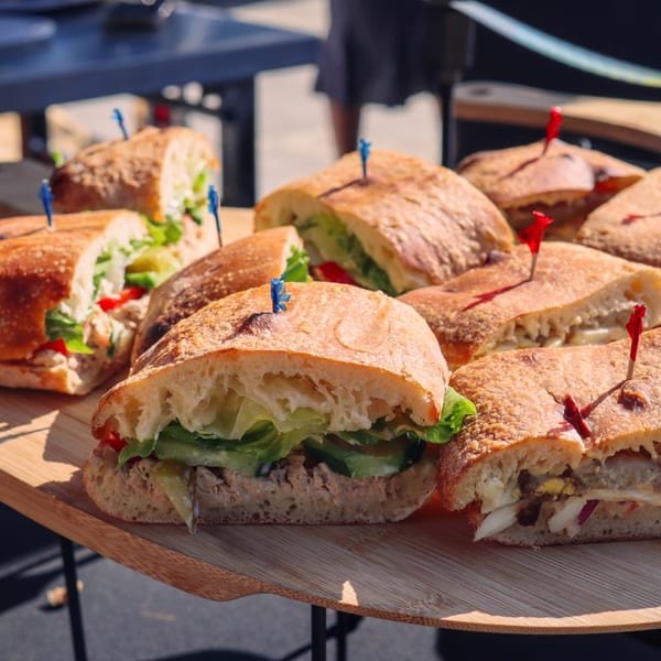 Assortment of fresh sandwiches with various fillings, cut in half and served on a wooden tray.