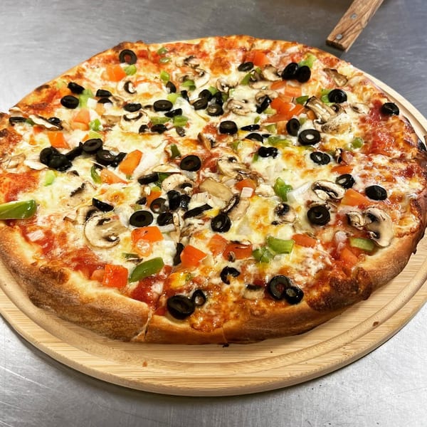 A whole Brami's Kosher Pizza with mushrooms, olives, green peppers, and tomatoes on a wooden board.