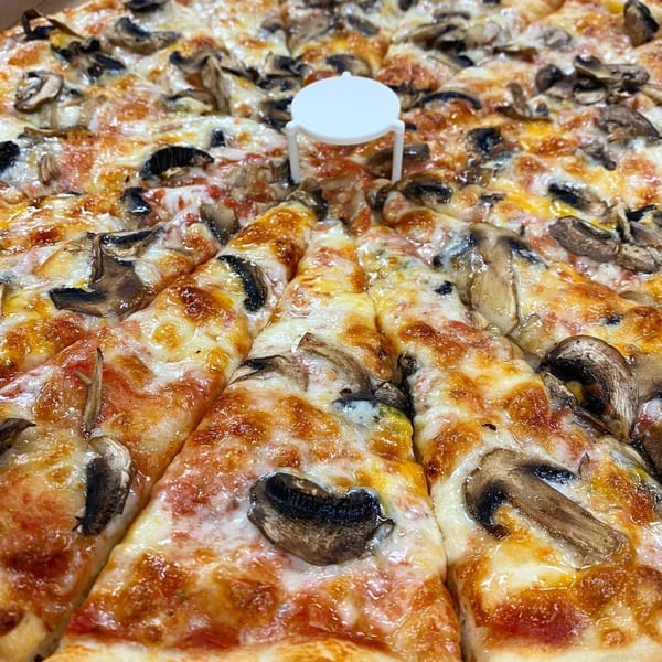 Close-up of a Brami's Kosher Pizza with mushrooms and melted cheese, sliced with a pizza saver.