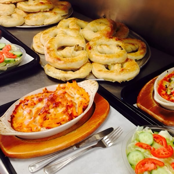 Baked ziti, fresh garden salad, and trays of golden-brown pretzels with sesame seeds at Brami's Kosher Pizza.
